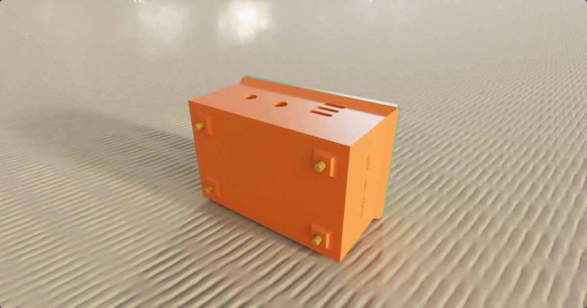 An orange machined box assembly on rippled sand